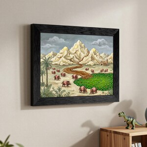 May include: Framed artwork depicting a whimsical landscape with mountains, a river, and a field of green. The painting features several pink and brown creatures. The artwork is framed in a black wooden frame.