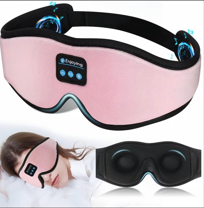 May include: A pink eye mask with a black strap and accents. The mask has the word "Enjoying" and control buttons. The image also shows a person wearing the mask and a black version of the mask.
