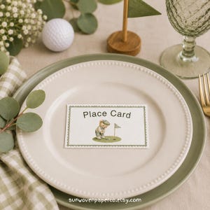 May include: A rectangular white place card with a scalloped green border, featuring the text "Place Card" and an illustration of a teddy bear playing golf. The card is centered on a cream-colored plate with a beaded edge, resting on a green plate.