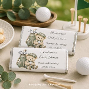 Pode incluir: Duas embalagens retangulares de barras de chocolate com uma ilustração em aguarela de um urso de peluche com um boné xadrez sentado junto a um saco de golfe. O texto diz Stephanie's Baby Shower, Thank you for coming! e 09.20.2026.