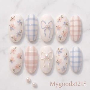 May include: A set of ten artificial nails with a variety of designs. Some nails feature a light blue and pink floral pattern, others have a plaid design in blue and pink, and some have a bow design with a pearl accent. The text "Mygoods1215" is visible.