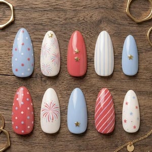 May include: A collection of ten artificial nails with various designs. The nails feature patterns like polka dots, stripes, fireworks, and stars in red, white, and blue colors. Some nails have gold star embellishments.