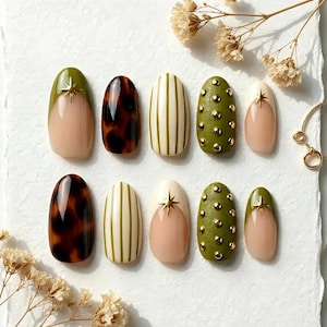 May include: A set of ten press-on nails featuring various designs including olive green French tips with gold star accents, brown tortoiseshell patterns, cream nails with olive green vertical stripes, and olive green nails with gold studs.
