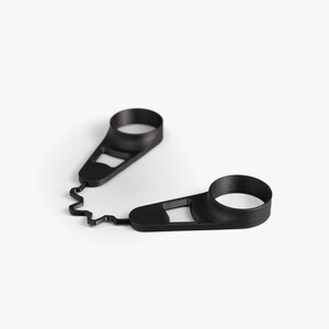 May include: Two black, 3D-printed wine bottle pourer rings connected by a wavy, zig-zag shaped piece. Each ring has a circular opening and a flat, rectangular base with a cutout. The pourer rings are designed to catch drips.