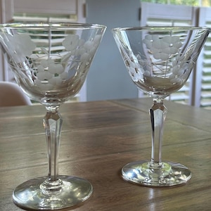 Pode incluir: Duas taças de cocktail em vidro transparente com um delicado padrão floral gravado na taça. Cada copo tem uma haste facetada de vários lados que conduz a uma base circular lisa, proporcionando uma base estável para o recipiente largo.