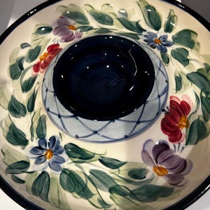 May include: A ceramic serving dish with a central dip bowl. The dish features a cream-colored background with hand-painted floral and leaf designs in red, purple, blue, and green. The rim and dip bowl are navy blue.
