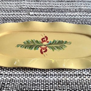 May include: An oval-shaped yellow serving tray with a wavy, scalloped edge. The center of the tray features a hand-painted decorative motif consisting of symmetrical green fern-like leaves and small red floral accents arranged horizontally.