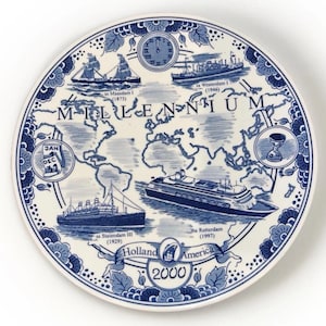 May include: A white ceramic plate with a blue and white design. The plate features a world map, ships, and the word "MILLENNIUM". The plate also has the text "Holland America" and the year "2000".