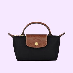May include: Black handbag with a brown leather flap and handle. The bag has a gold zipper and a gold button closure on the flap. The bag is a tote style and has a simple, elegant design.