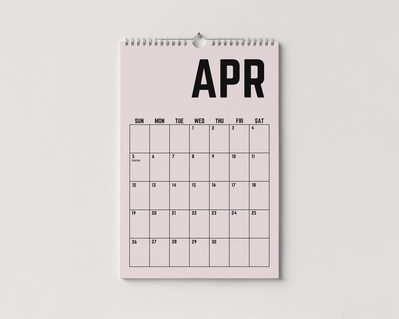 Peut inclure: Un calendrier mural rose clair pour le mois d'avril, avec du texte noir. Le mot "APR" est en haut, avec une grille de dates en dessous. Le calendrier est maintenu par une reliure en spirale argent&eacute;e et un petit trou pour l'accrocher.