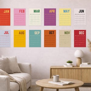 Pode incluir: Uma cole&ccedil;&atilde;o de doze calend&aacute;rios mensais coloridos, cada um com uma cor de fundo diferente e o nome do m&ecirc;s no topo. Os calend&aacute;rios s&atilde;o exibidos em uma parede em uma sala de estar, com m&oacute;veis e decora&ccedil;&atilde;o vis&iacute;veis.