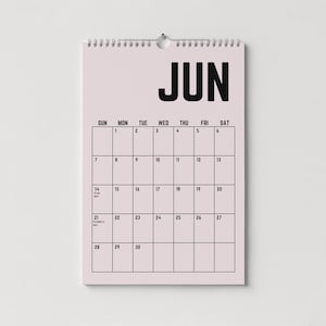 Peut inclure: Un calendrier mural de juin, avec un fond rose clair et du texte noir. Le mot "JUN" est en haut, avec les jours de la semaine en haut. La grille du calendrier est soulign&eacute;e en noir, avec les dates et les jours sp&eacute;ciaux not&eacute;s.
