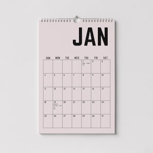 Peut inclure: Calendrier mural de janvier avec un fond rose clair et du texte noir. Le mot "JAN" est en haut, avec une grille de dates en dessous. Il a une reliure en spirale argent&eacute;e et un trou pour l'accrocher. Id&eacute;al pour planifier.