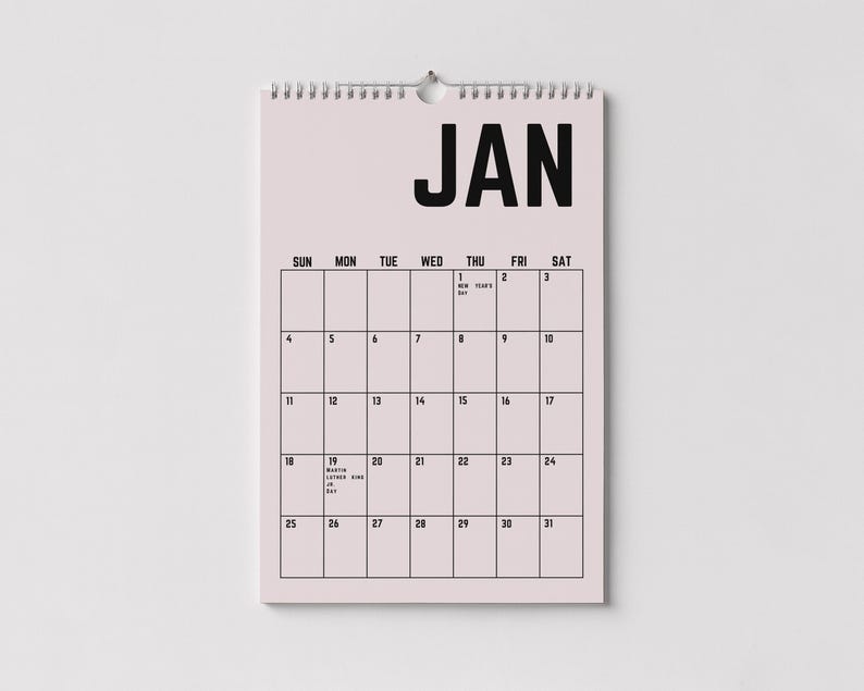 Peut inclure: Calendrier mural de janvier avec un fond rose clair et du texte noir. Le mot "JAN" est en haut, avec une grille de dates en dessous. Il a une reliure en spirale argent&eacute;e et un trou pour l'accrocher. Id&eacute;al pour planifier.