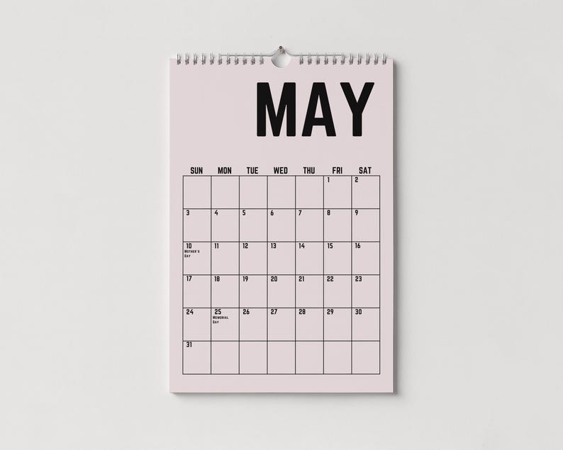 Peut inclure: Calendrier mural de mai avec un fond rose clair et du texte noir. Le mot "MAI" est en haut, avec les jours de la semaine en dessous. La grille du calendrier est visible, avec les dates et les jours f&eacute;ri&eacute;s marqu&eacute;s.