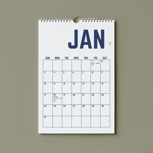 May include: A white wall calendar for January 2017, hanging against a muted green background. The calendar features a grid layout with the days of the week across the top and dates in blue. The word "JAN" is prominently displayed at the top.