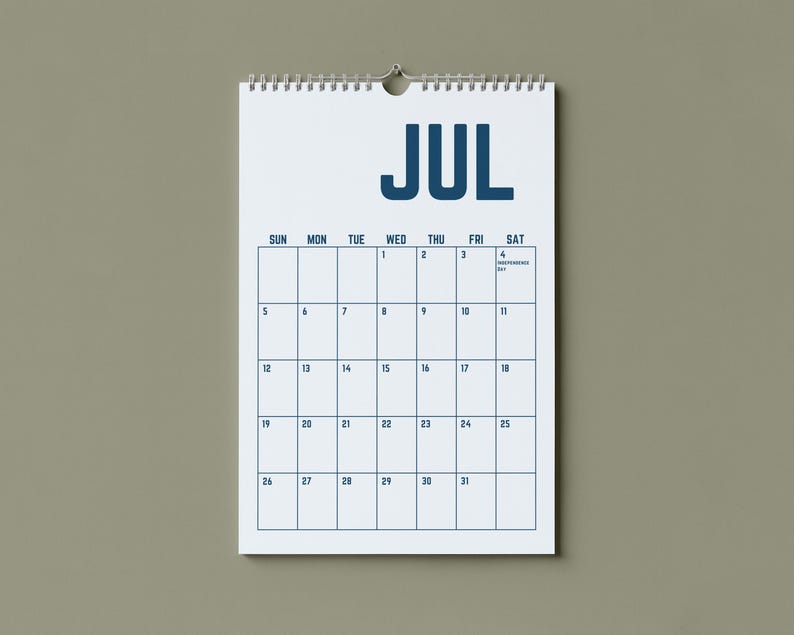 May include: A white spiral-bound calendar for July hangs against a neutral background. The word "JUL" is printed in bold, dark blue letters at the top. The calendar grid is outlined in dark blue, with dates and days of the week.