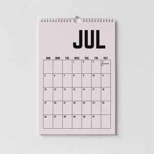 Peut inclure: Calendrier mural de juillet, reli&eacute; par une spirale en haut. Le mot "JUL" est en noir gras. La grille du calendrier affiche les jours de la semaine et les dates, avec le 4 marqu&eacute; comme Jour de l'Ind&eacute;pendance.