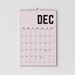 Peut inclure: Un calendrier mural de d&eacute;cembre, avec un fond rose clair et du texte noir. Le mot "DEC" est en haut, avec les jours de la semaine et les dates en dessous. Le calendrier est reli&eacute; par une spirale argent&eacute;e.
