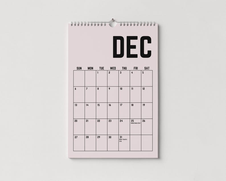 Peut inclure: Un calendrier mural de d&eacute;cembre, avec un fond rose clair et du texte noir. Le mot "DEC" est en haut, avec les jours de la semaine et les dates en dessous. Le calendrier est reli&eacute; par une spirale argent&eacute;e.