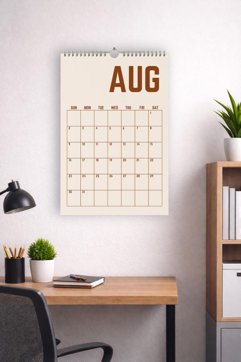 May include: A wall calendar for August, with a cream-colored background and brown grid lines. The word "AUG" is at the top. The calendar is hanging above a wooden desk with a black desk lamp and a small potted plant.