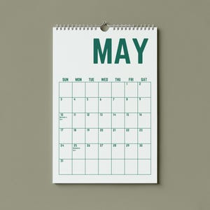 May include: A white spiral-bound calendar for the month of May, hanging against a neutral background. The word "MAY" is printed in bold, dark green letters at the top. The calendar grid is outlined in green, with dates and days of the week.