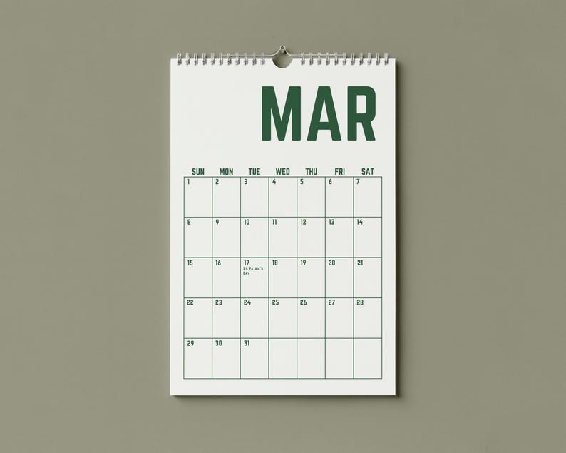 May include: A white spiral-bound calendar for the month of March, hanging against a muted green background. The word "MAR" is printed in bold, dark green letters at the top. The calendar grid is outlined in dark green, with dates and days of the week.