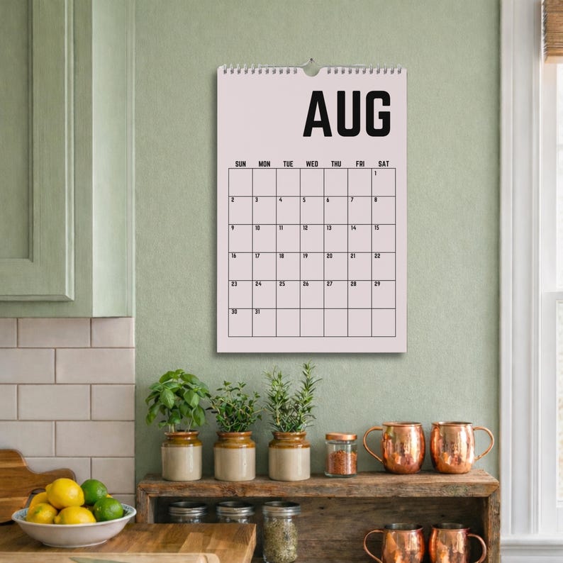 Peut inclure: Un calendrier d'ao&ucirc;t rose clair est accroch&eacute; au mur au-dessus d'une &eacute;tag&egrave;re en bois avec des mugs en cuivre et des plantes en pot. Le calendrier affiche les jours du mois en texte noir. Le mot "AUG" est en haut du calendrier.