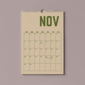 Pode incluir: Um calend&aacute;rio de parede bege para novembro, com encaderna&ccedil;&atilde;o em espiral no topo. A palavra "NOV" &eacute; impressa em letras verdes grandes. A grelha do calend&aacute;rio &eacute; num estilo simples e minimalista, com datas e dias da semana.