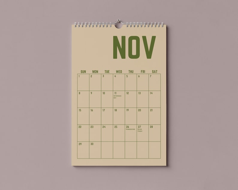 Pode incluir: Um calend&aacute;rio de parede bege para novembro, com encaderna&ccedil;&atilde;o em espiral no topo. A palavra "NOV" &eacute; impressa em letras verdes grandes. A grelha do calend&aacute;rio &eacute; num estilo simples e minimalista, com datas e dias da semana.