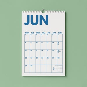 Pu&ograve; includere: Un calendario da parete per il mese di giugno con sfondo bianco e testo blu in grassetto. Il calendario presenta una griglia con i giorni della settimana, date numerate da 1 a 30 e piccoli testi per Flag Day e Father's Day, rilegato con una spirale.