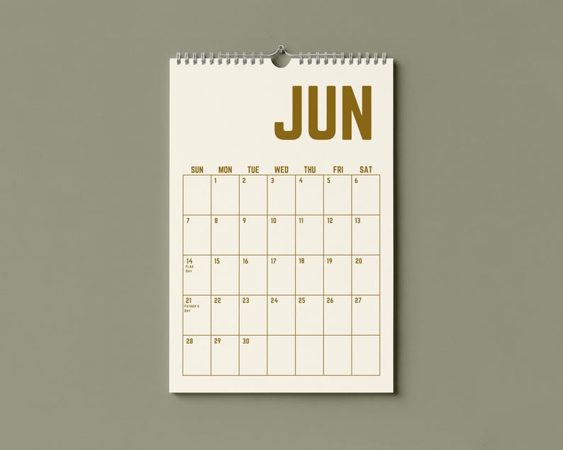 May include: A cream-colored wall calendar for June, with a spiral binding and a metal hook for hanging. The word "JUN" is printed in large, bold, gold letters at the top. The calendar grid features dates and days of the week in a simple, readable font.