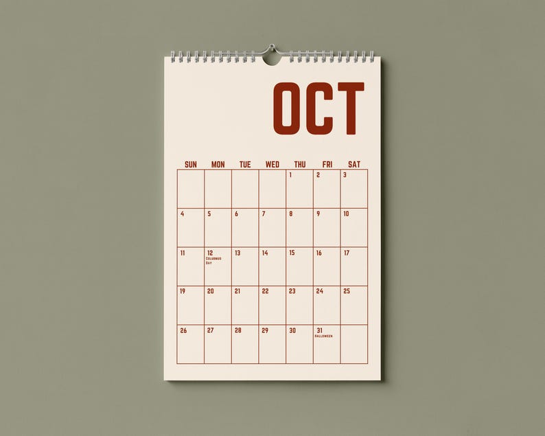 May include: A cream-colored wall calendar for October, with a spiral binding and a metal hook for hanging. The word "OCT" is printed in bold, dark red letters at the top. The calendar grid is outlined in dark red, with dates and days of the week.