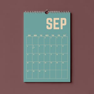 Pode incluir: Um calend&aacute;rio de parede azul-petr&oacute;leo para setembro, com o nome do m&ecirc;s em letras grandes e em negrito. A grelha do calend&aacute;rio &eacute; de cor bege claro, com os dias da semana no topo. O calend&aacute;rio est&aacute; pendurado numa parede castanha.