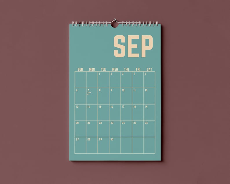 Pode incluir: Um calend&aacute;rio de parede azul-petr&oacute;leo para setembro, com o nome do m&ecirc;s em letras grandes e em negrito. A grelha do calend&aacute;rio &eacute; de cor bege claro, com os dias da semana no topo. O calend&aacute;rio est&aacute; pendurado numa parede castanha.