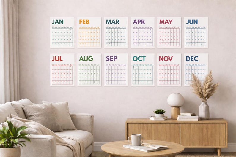 Pu&ograve; includere: Un set di dodici stampe di calendario da parete disposte su due file, ognuna con il nome del mese in un colore distinto e una griglia dei giorni. I mesi da JAN a DEC sono visualizzati con testo colorato e linee di griglia nere su carta.