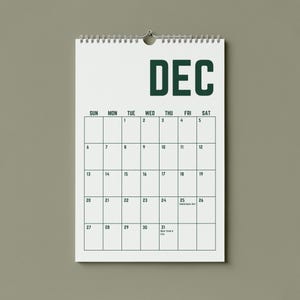 May include: A white wall calendar for December, hanging against a muted green background. The word "DEC" is printed in dark green at the top. The calendar grid is outlined in dark green, with dates and days of the week displayed.