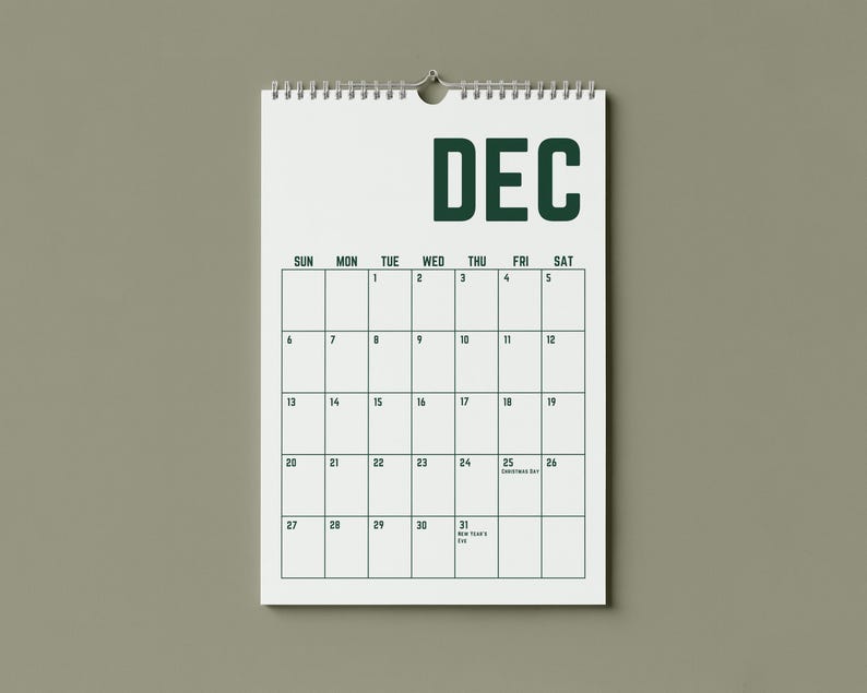 May include: A white wall calendar for December, hanging against a muted green background. The word "DEC" is printed in dark green at the top. The calendar grid is outlined in dark green, with dates and days of the week displayed.