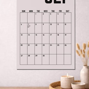 Peut inclure: Un calendrier mural de septembre avec un fond rose clair. Le mot "SEP" est en lettres noires en gras en haut. La grille du calendrier est noire avec les dates et les jours de la semaine. Une bougie, un bol et un vase sont sur une surface en bois.