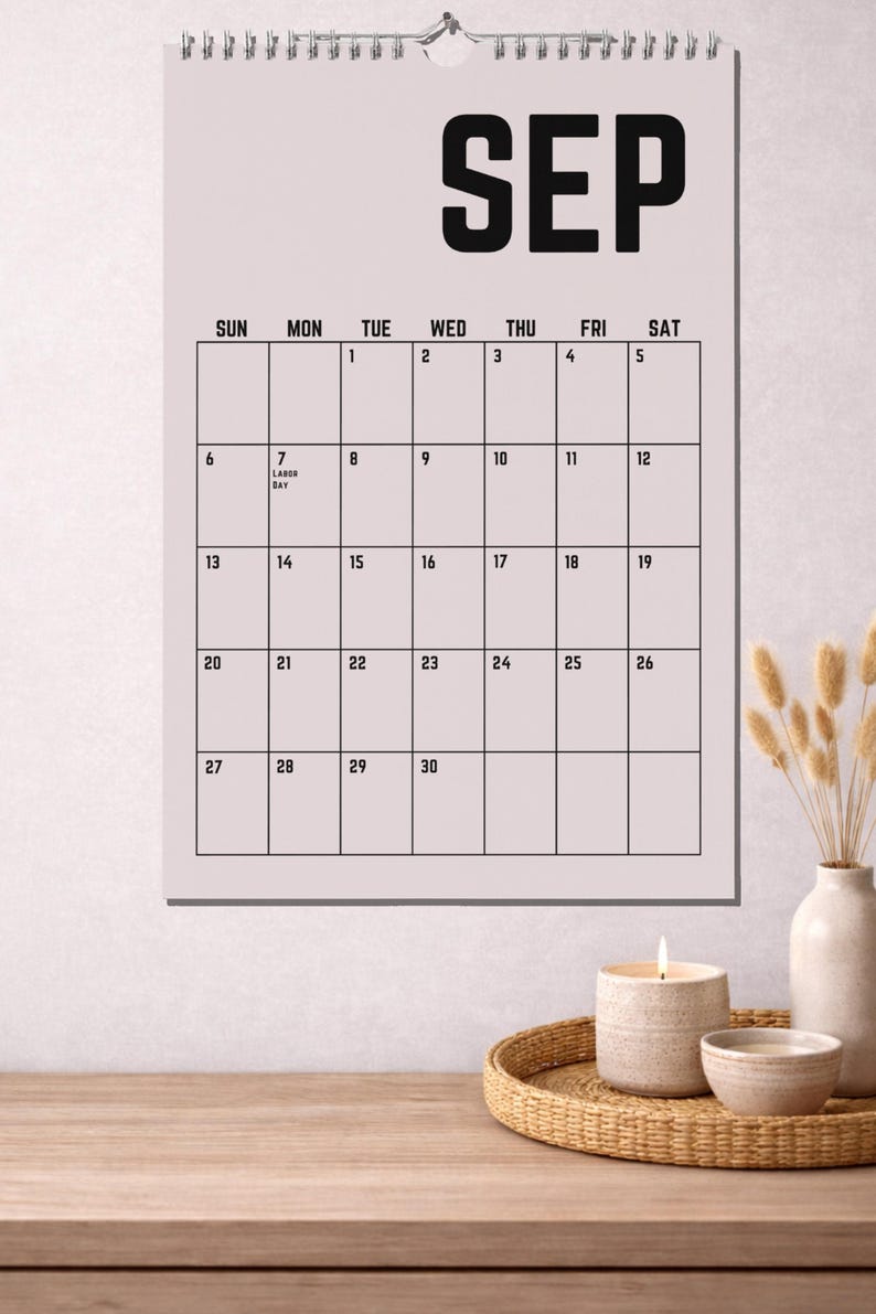 Peut inclure: Un calendrier mural de septembre avec un fond rose clair. Le mot "SEP" est en lettres noires en gras en haut. La grille du calendrier est noire avec les dates et les jours de la semaine. Une bougie, un bol et un vase sont sur une surface en bois.