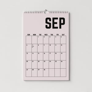 Peut inclure: Un calendrier mural pour le mois de septembre avec un fond rose clair et du texte noir. Le mot "SEP" est en haut, avec les jours de la semaine et les dates en dessous. Le calendrier est reli&eacute; par une spirale argent&eacute;e.