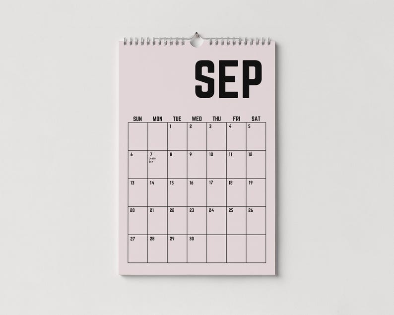 Peut inclure: Un calendrier mural pour le mois de septembre avec un fond rose clair et du texte noir. Le mot "SEP" est en haut, avec les jours de la semaine et les dates en dessous. Le calendrier est reli&eacute; par une spirale argent&eacute;e.