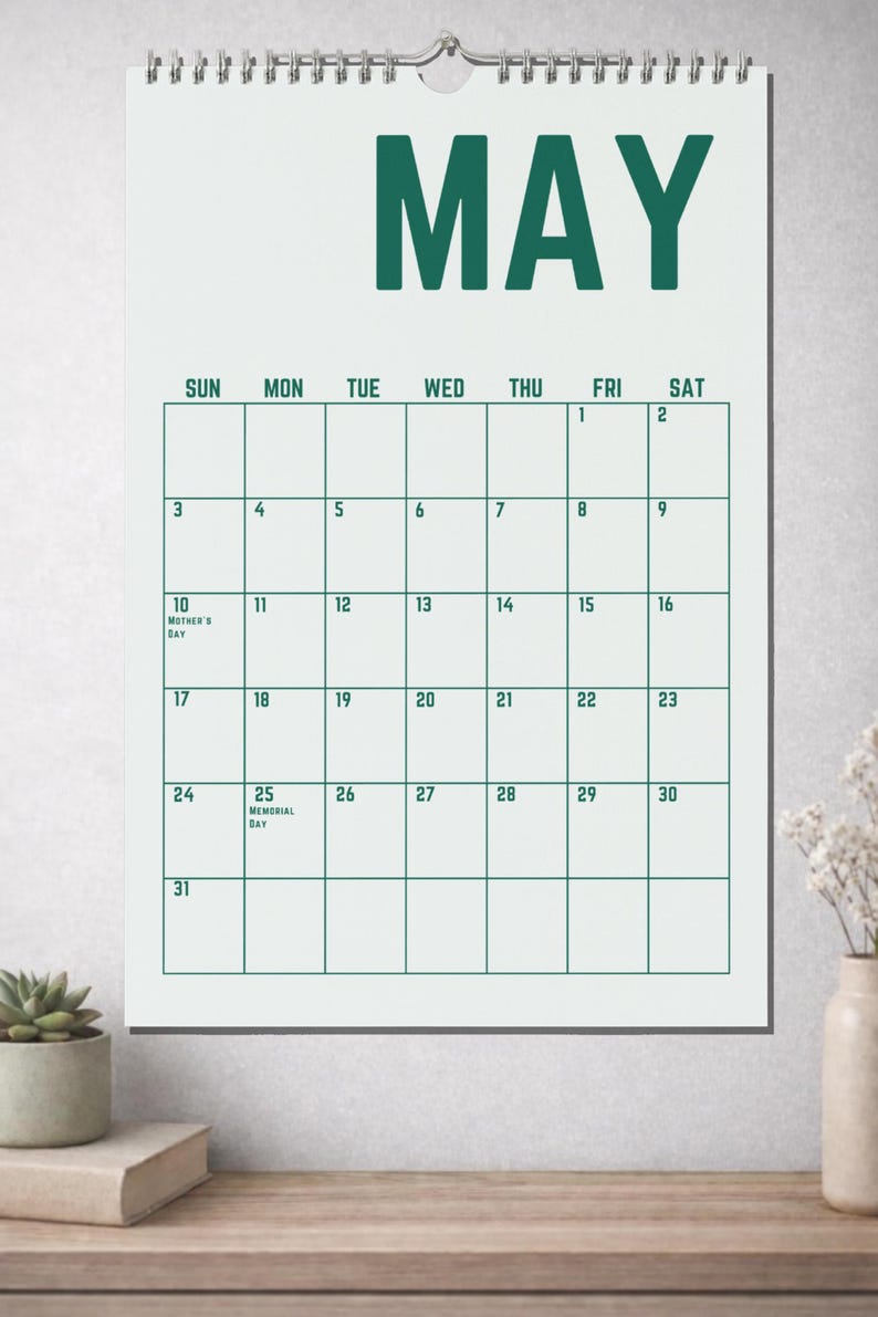 May include: A white wall calendar for the month of May, with a green font. The calendar grid is outlined in green. The 10th is labeled "Mother's Day" and the 25th is labeled "Memorial Day".
