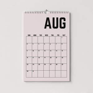 Peut inclure: Calendrier mural rose clair pour le mois d'ao&ucirc;t. Le mot "AUG" est en haut, en noir, au-dessus d'une grille de dates. Le calendrier est reli&eacute; par une spirale en haut et est suspendu &agrave; une boucle m&eacute;tallique.