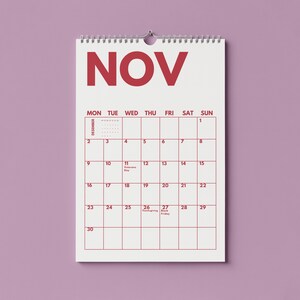 Pu&ograve; includere: Un calendario da parete per il mese di novembre con sfondo bianco e testo rosso. Il calendario presenta una disposizione a griglia con i giorni della settimana, le date dall'1 al 30 e specifiche etichette per festivit&agrave; come Veterans Day.