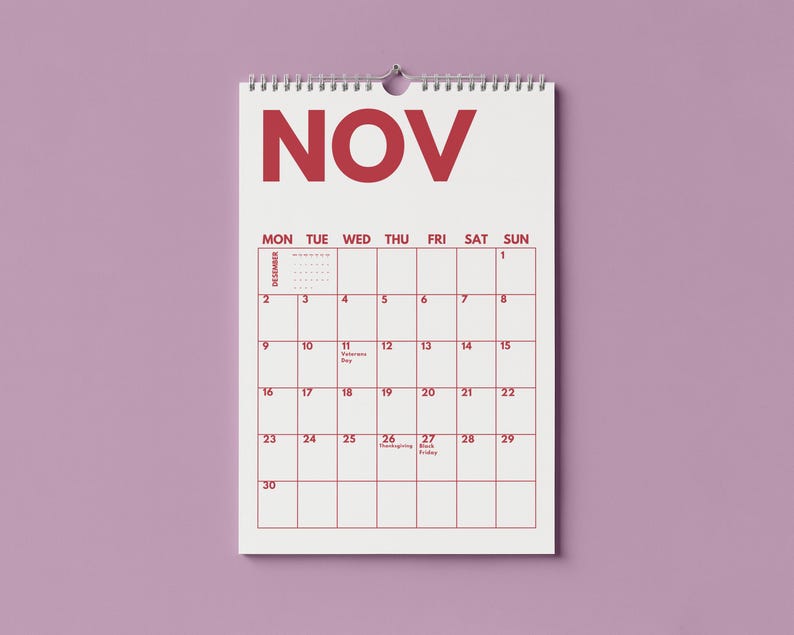 Pu&ograve; includere: Un calendario da parete per il mese di novembre con sfondo bianco e testo rosso. Il calendario presenta una disposizione a griglia con i giorni della settimana, le date dall'1 al 30 e specifiche etichette per festivit&agrave; come Veterans Day.