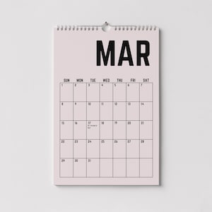 Peut inclure: Un calendrier mural rose pour le mois de mars avec du texte noir. Le mot "MAR" est en haut, avec une grille de dates en dessous. Le calendrier est accroch&eacute; &agrave; un mur blanc.