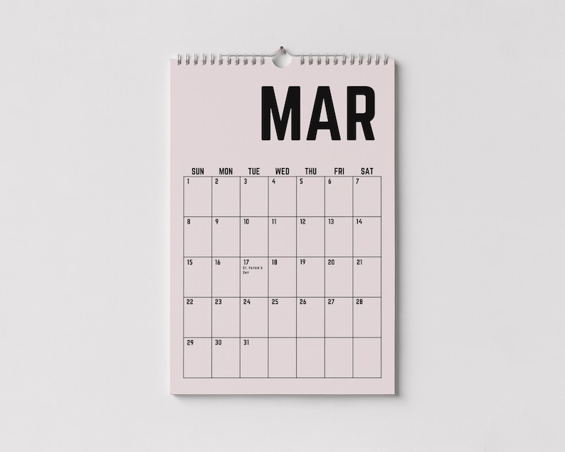 Peut inclure: Un calendrier mural rose pour le mois de mars avec du texte noir. Le mot "MAR" est en haut, avec une grille de dates en dessous. Le calendrier est accroch&eacute; &agrave; un mur blanc.