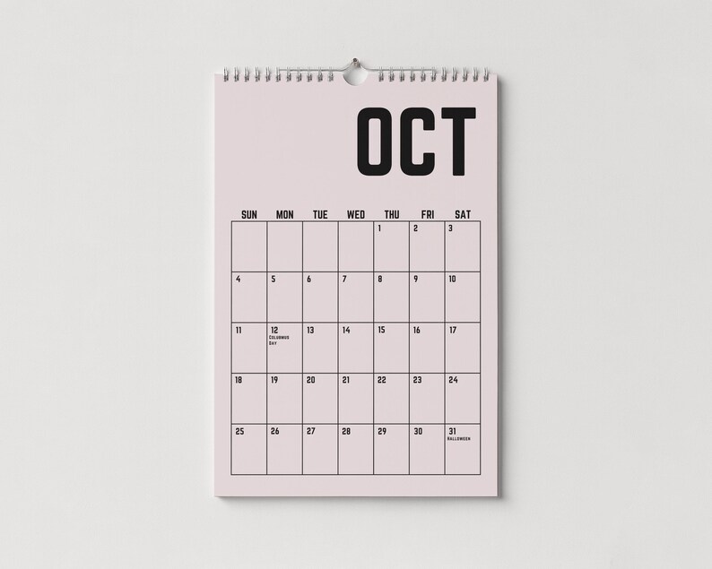 Peut inclure: Un calendrier mural rose pour le mois d'octobre, avec une reliure &agrave; spirale en haut. Le mot "OCT" est imprim&eacute; en lettres noires en gras. La grille du calendrier affiche les jours du mois, avec les dates et quelques jours sp&eacute;ciaux.