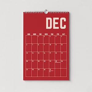 Pode incluir: Um calend&aacute;rio de parede vermelho para dezembro, com uma grade de datas e dias da semana. A palavra "DEC" est&aacute; no topo em letras brancas. O calend&aacute;rio est&aacute; pendurado em uma parede branca.